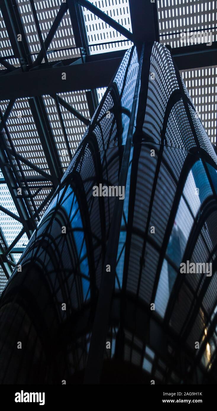 Low angle view of a shiny metal column inside a contemporary building, reflecting the metal and glass structure above. Stock Photo
