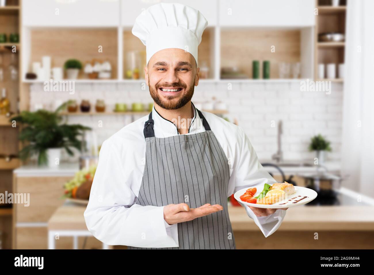 Happy Cook Man Presenting Dish Holding Plate Standing In Kitchen Stock Photo