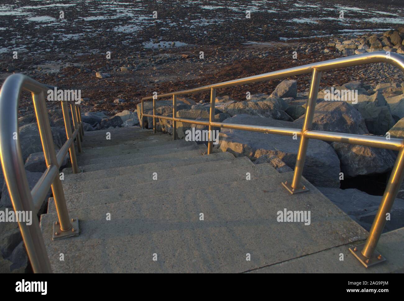 Looking down beach steps from the defensive wall, stainless steel railing and the tide is out. Stock Photo