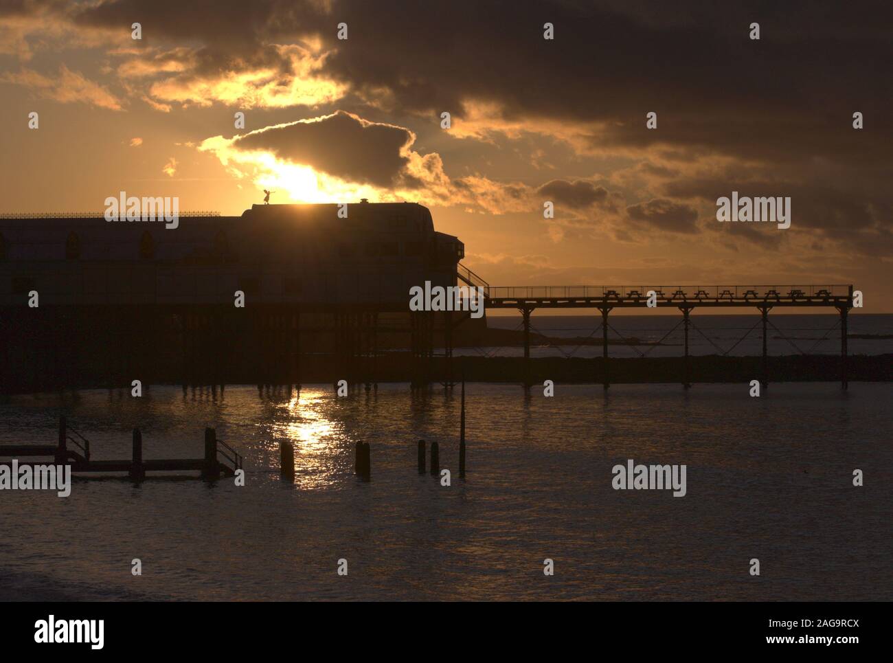 Grade II listed Wales's oldest pier built in 1864 by Eugenius Birch, shown in silhouette with the setting sky and the Angel of the war memorial. Stock Photo