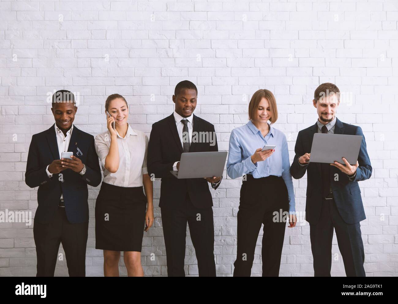 Young diverse team using modern gadgets, near white brick wal Stock Photo