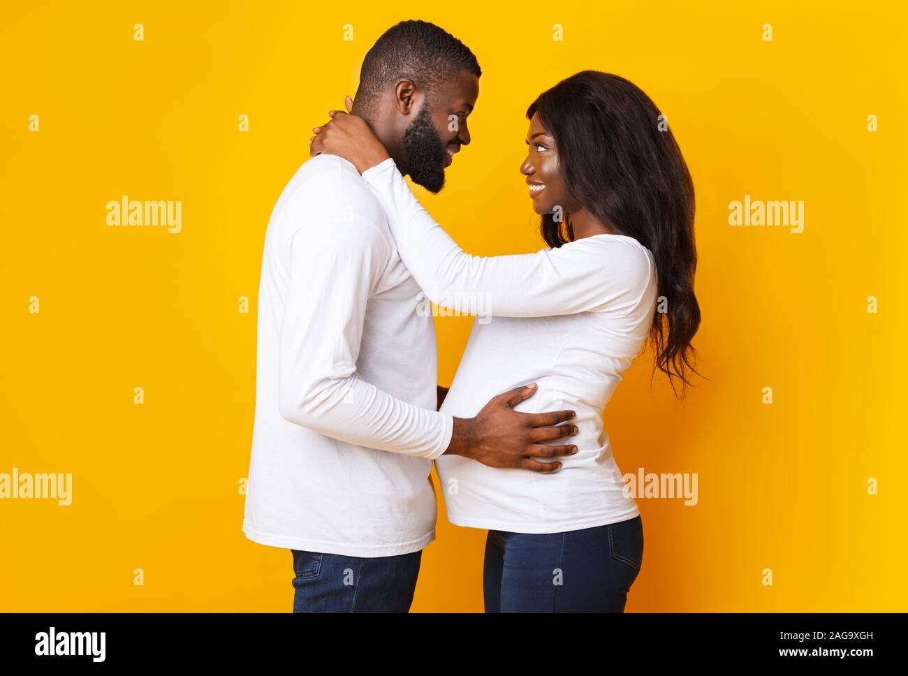Pregnant black woman and her husband embracing over yellow background Stock Photo