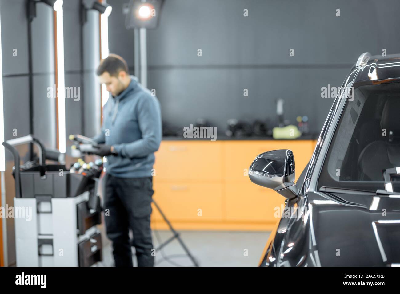 Car service worker preparing for vehicle body detailing at the modern automotive service box. Image focused on the car window Stock Photo