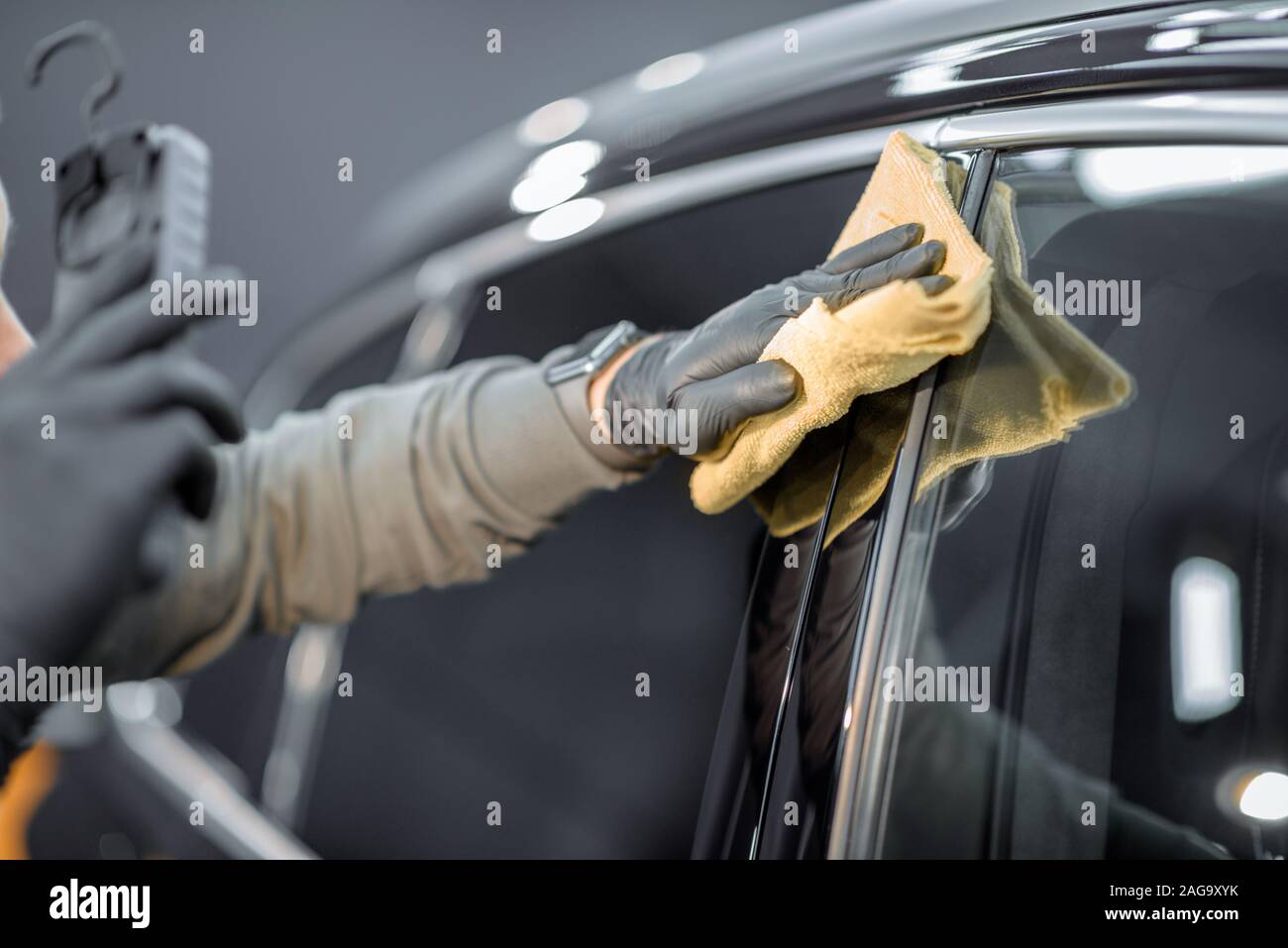 Car service worker wiping vehicle body with microfiber, examining glossy coating after the polishing procedure. Professional car detailing and maintenance concept Stock Photo