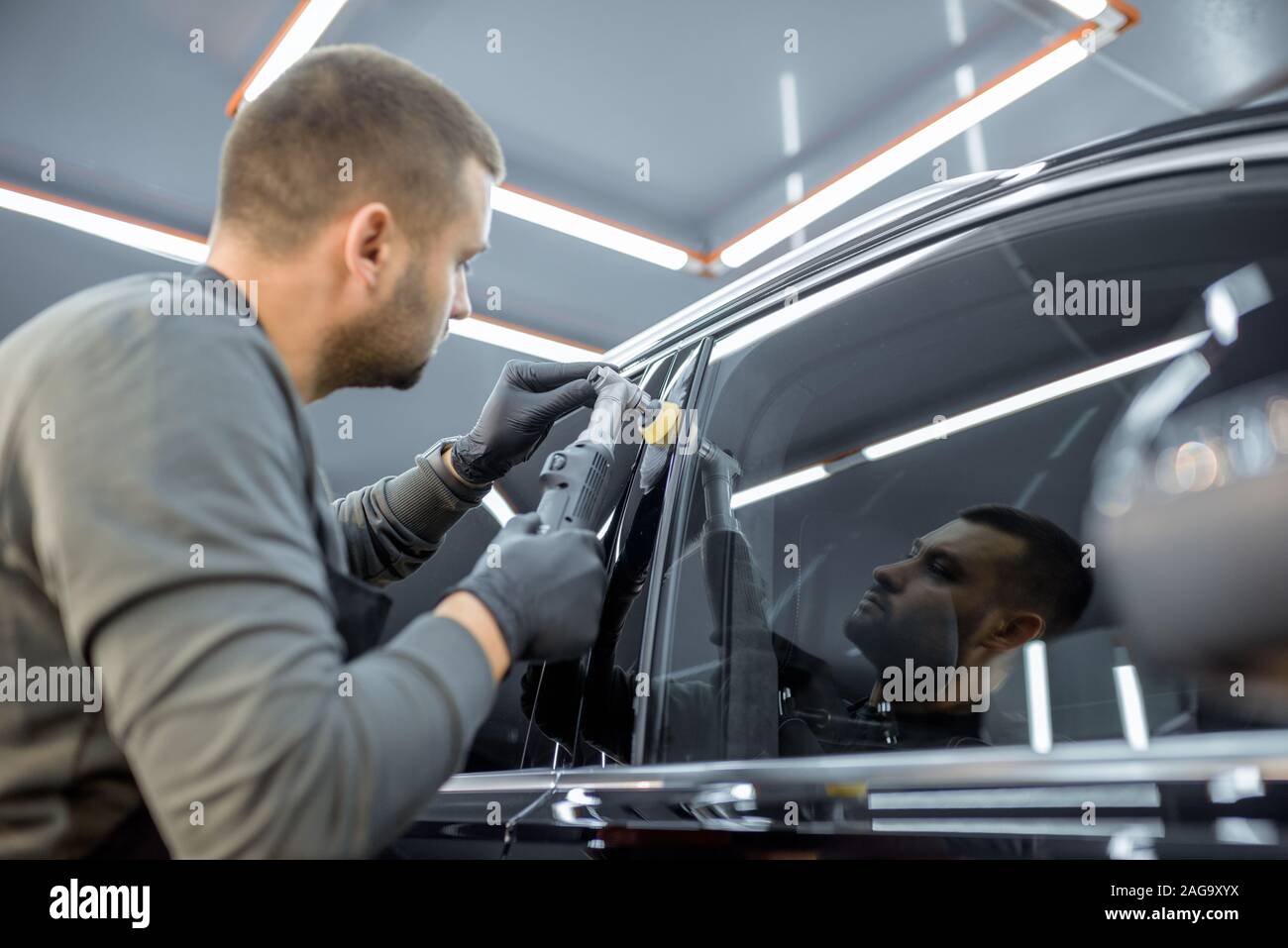 Car service worker polishing vehicle body with special wax from scratches. Professional car detailing and maintenance concept Stock Photo