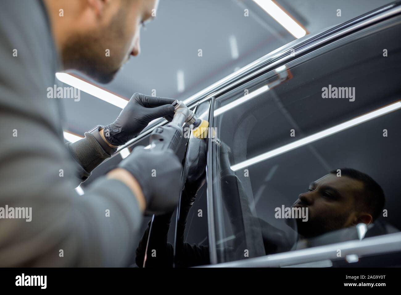 Car service worker polishing vehicle body with special wax from scratches. Professional car detailing and maintenance concept Stock Photo