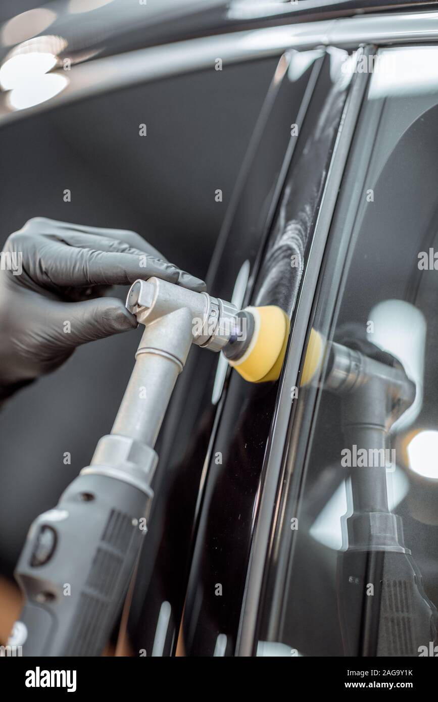 Car service worker polishing vehicle body with special wax from scratches, close-up. Professional car detailing and maintenance concept Stock Photo