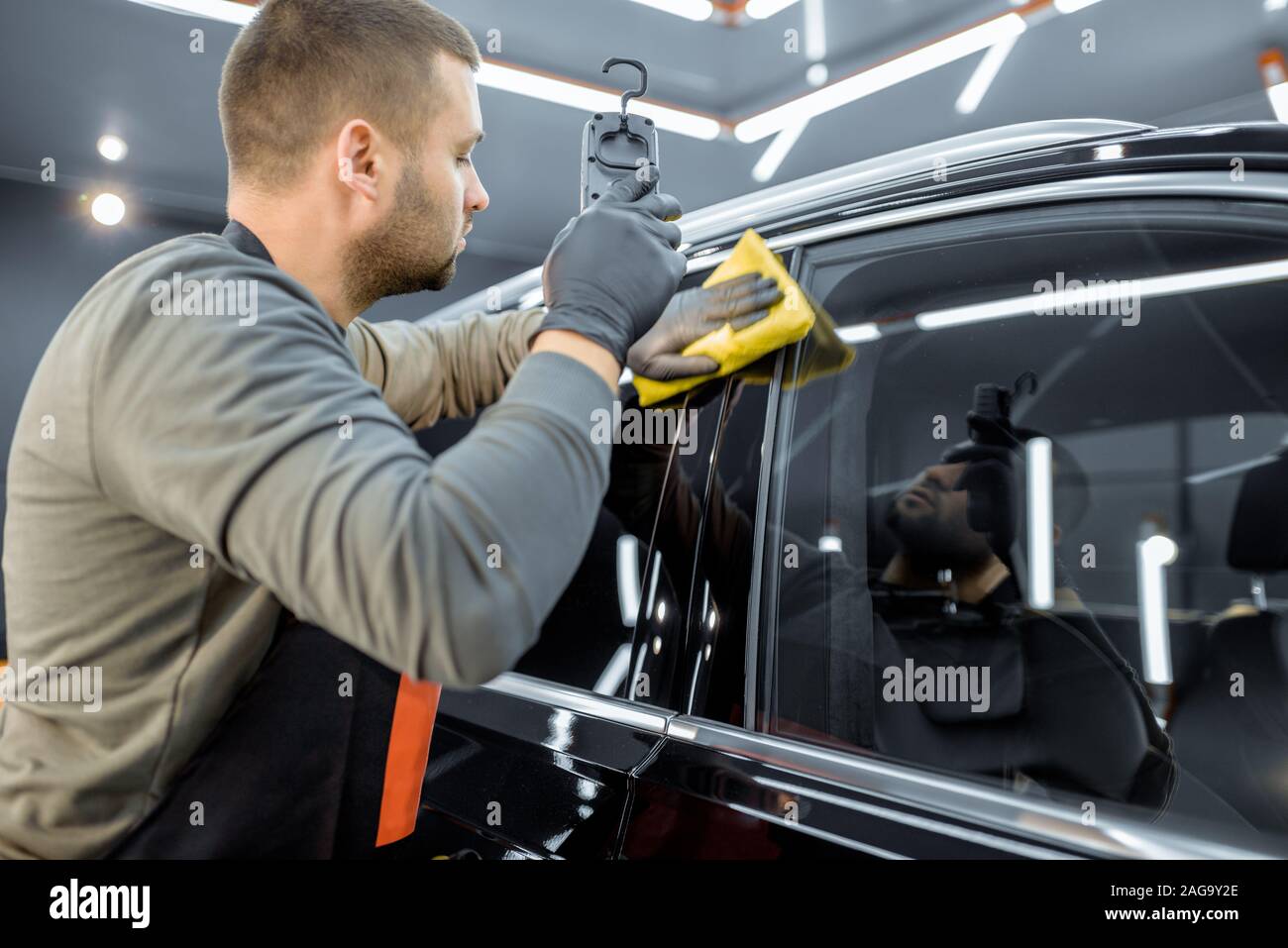 Car service worker wiping vehicle body with microfiber, examining glossy coating after the polishing procedure. Professional car detailing and maintenance concept Stock Photo
