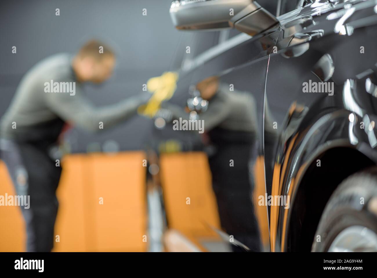 Car service worker wiping vehicle body with microfiber, examining glossy coating after the polishing procedure. Man blurred on the background Stock Photo