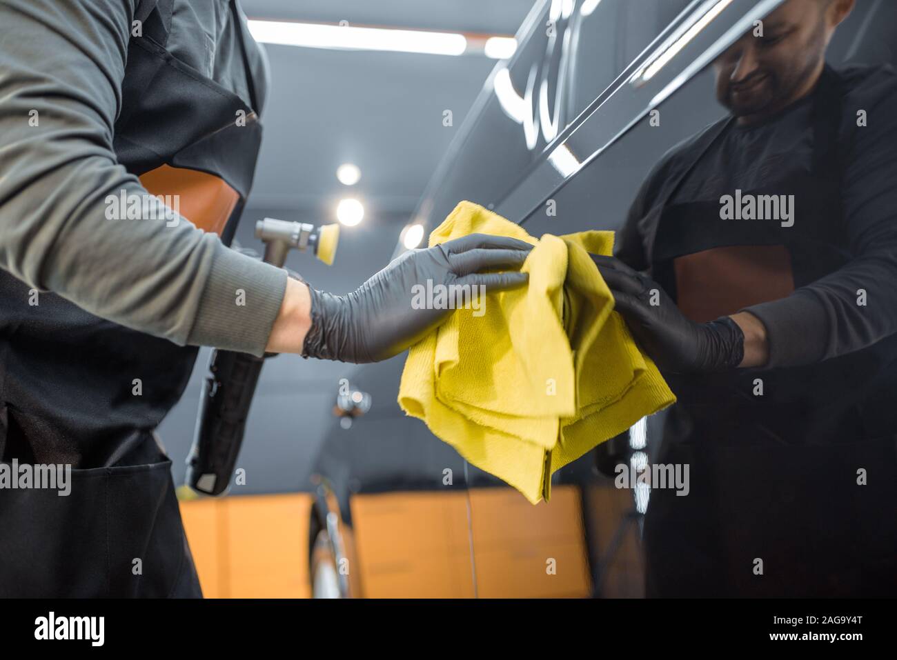 Car service worker wiping vehicle body with microfiber, examining glossy coating after the polishing procedure. Professional car detailing and maintenance concept Stock Photo