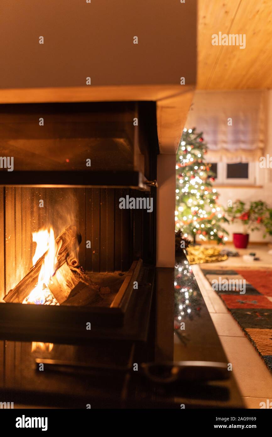 Firewood burning inside a fireplace with the decorated Christmas tree in the background Stock Photo