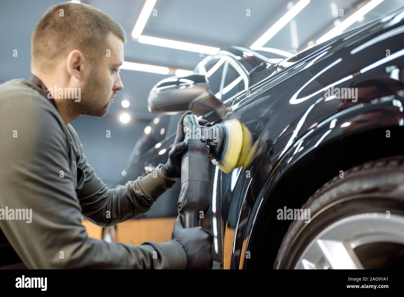 Worker polishing vehicle body with special grinder and wax from scratches at the car service station. Professional car detailing and maintenance concept Stock Photo