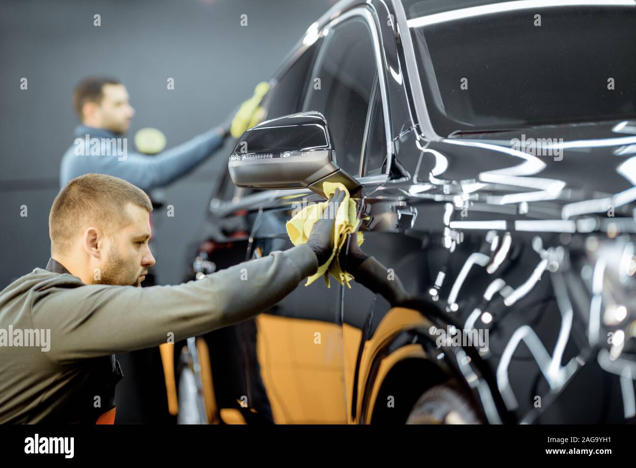 Car service workers wiping vehicle body with microfiber, examining glossy coating after the polishing procedure. Professional car detailing and maintenance concept Stock Photo