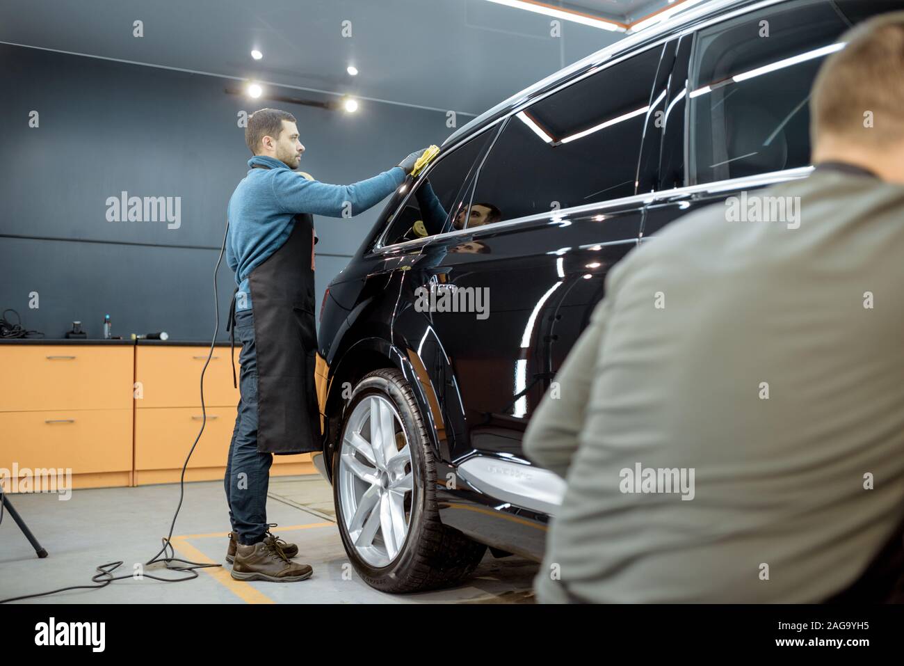 Car service workers wiping vehicle body with microfiber, examining glossy coating after the polishing procedure. Professional car detailing and maintenance concept Stock Photo