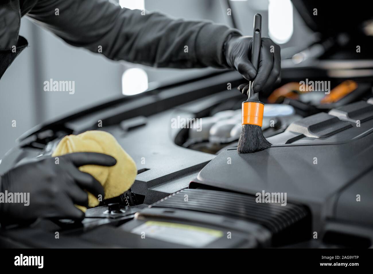 Man performs a professional car cleaning, washing engine with brush and