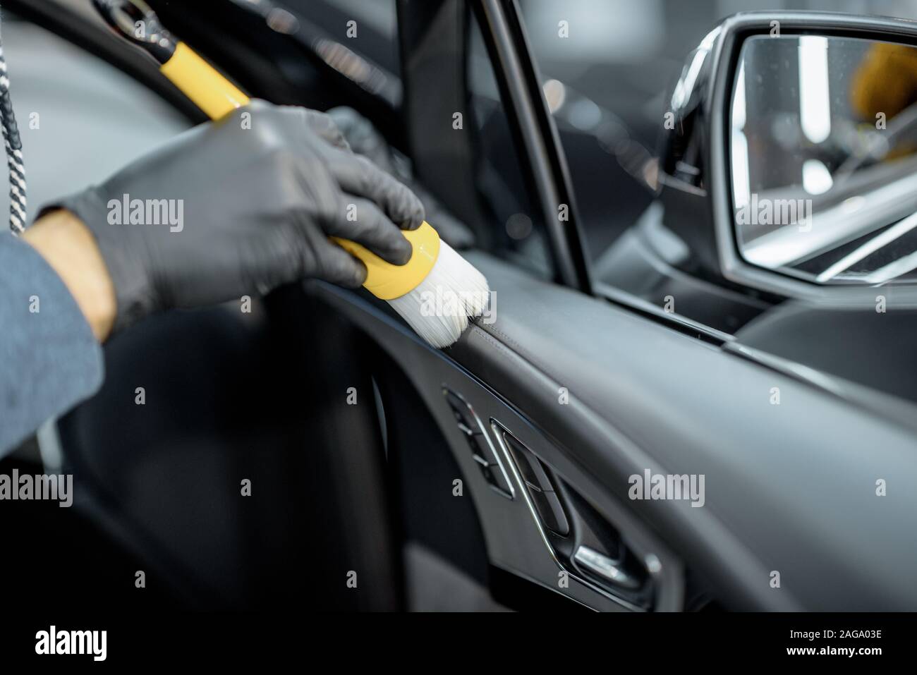 Worker provides a professional vehicle interior cleaning, wiping door panel with a brush at the car service station, close-up view Stock Photo