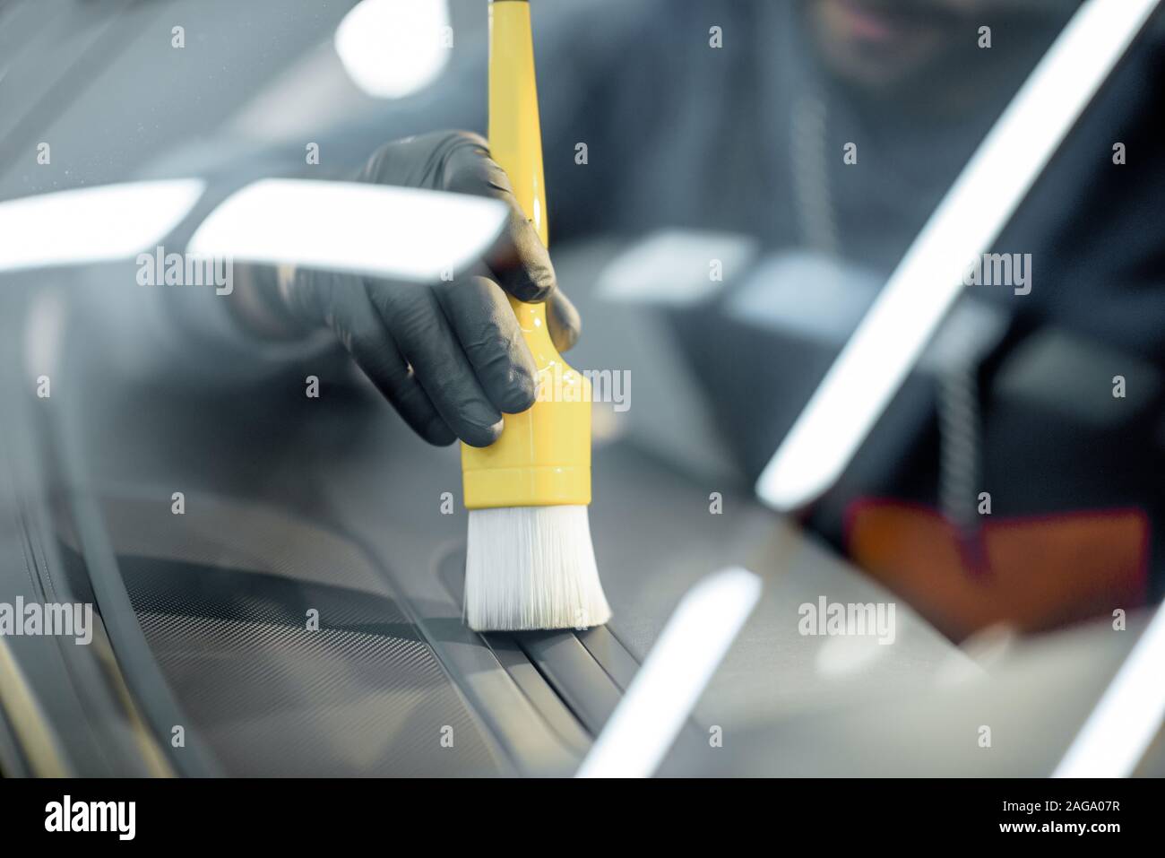 Worker provides a professional vehicle interior cleaning, wiping indoor front panel with a brush at the car service station, close-up Stock Photo