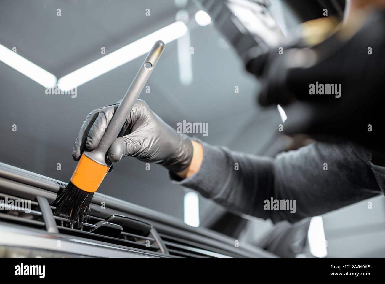 Worker provides a professional vehicle interior cleaning, wiping indoor front panel with a brush at the car service station, close-up Stock Photo