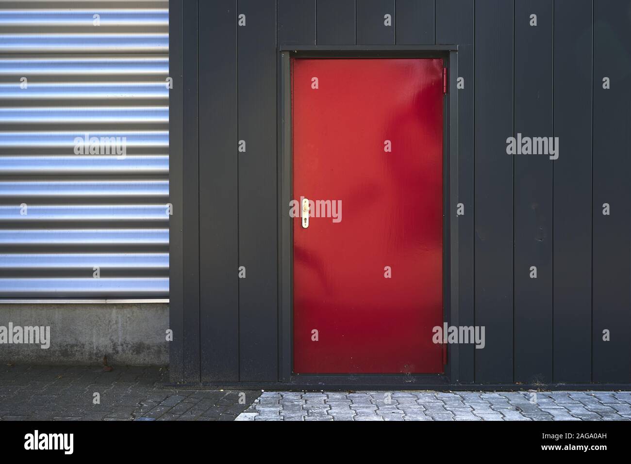 Building with black and silver walls and a red door on the pavement