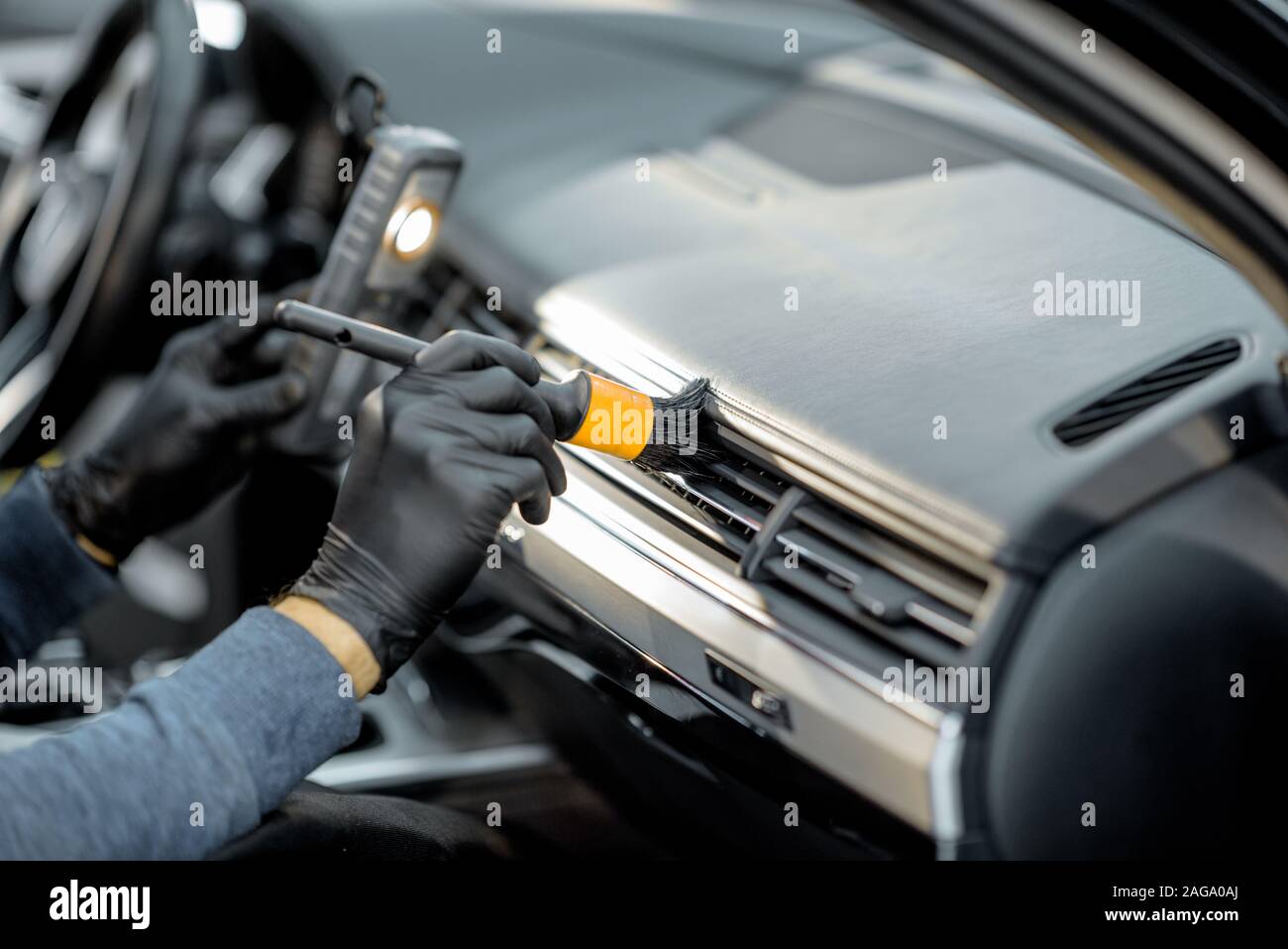 Worker provides a professional vehicle interior cleaning, wiping indoor front panel with a brush at the car service station, close-up Stock Photo