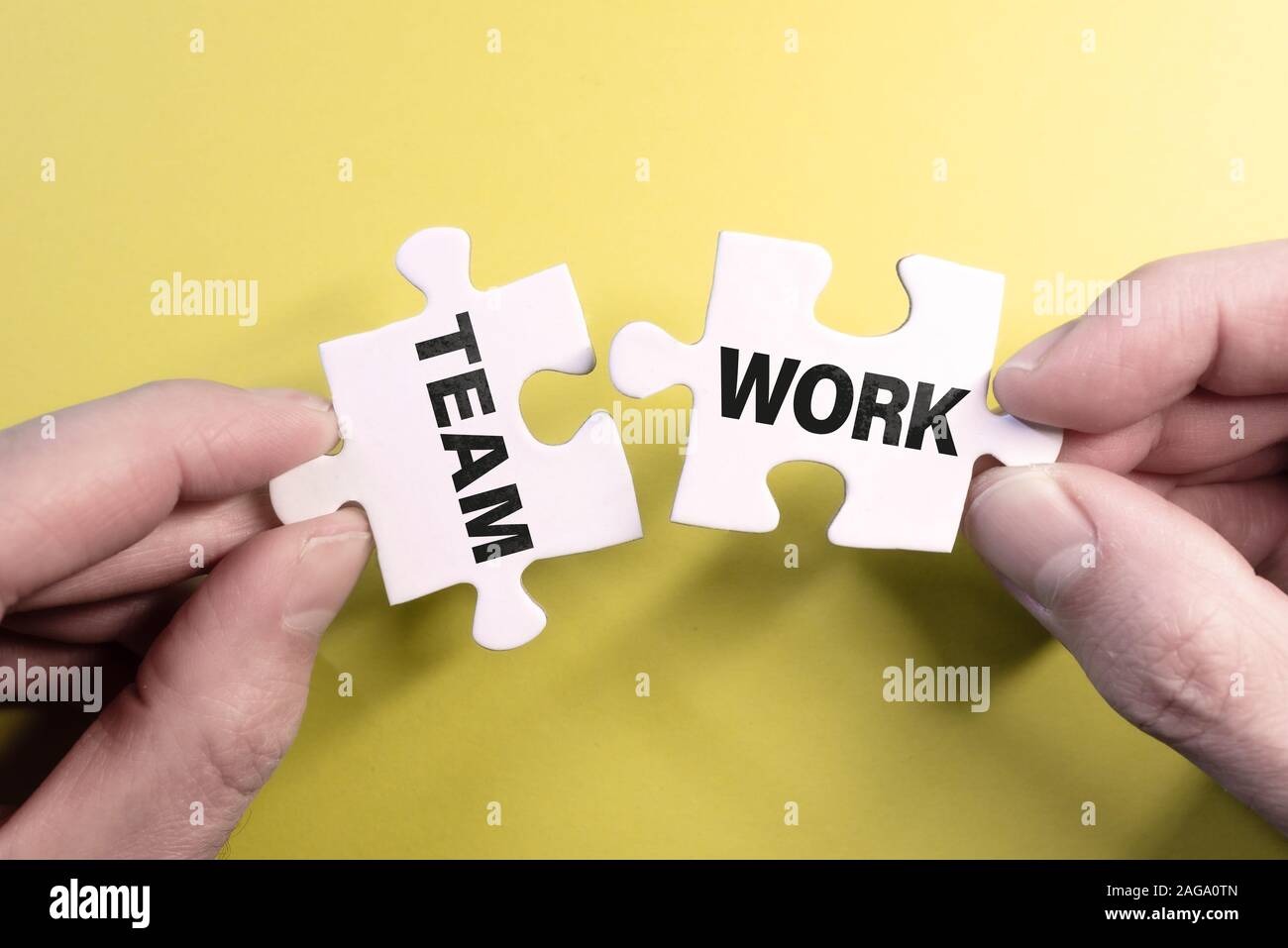teamwork concept with hand connecting puzzle pieces against yellow background Stock Photo