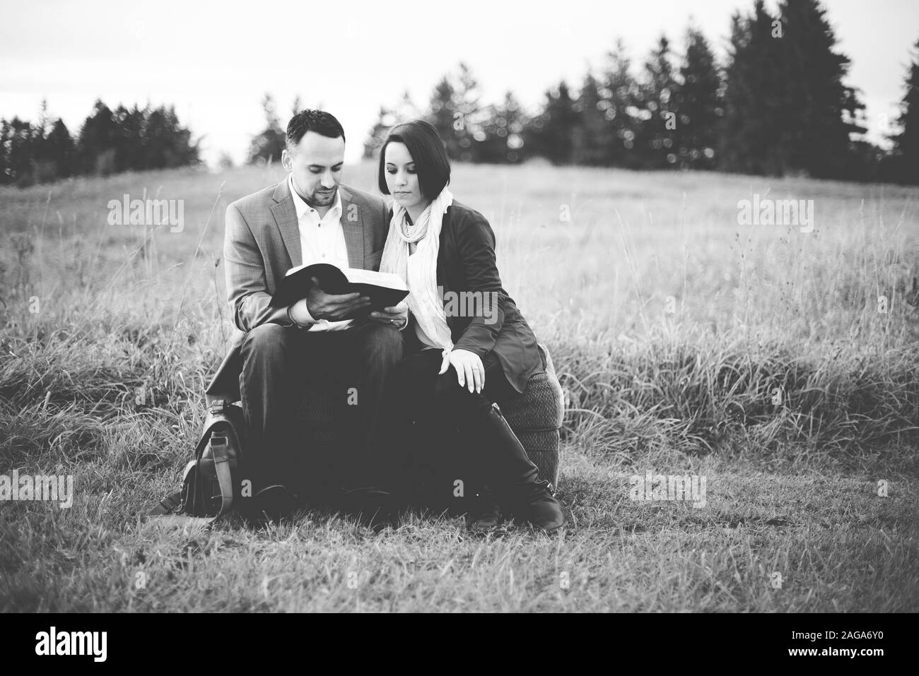 Grayscale shot of a couple sitting and reading the bible Stock Photo