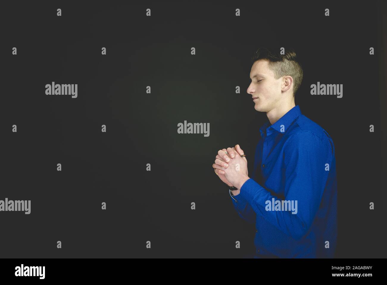 Male praying while his eyes are closed with a black background Stock Photo