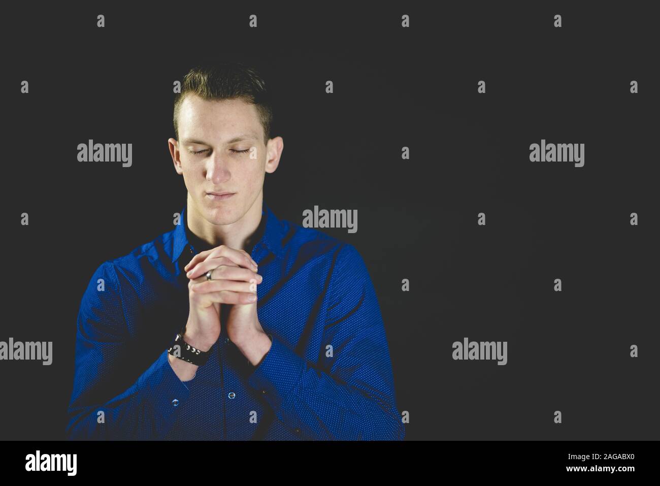 Male praying while his eyes are closed with a black background Stock Photo