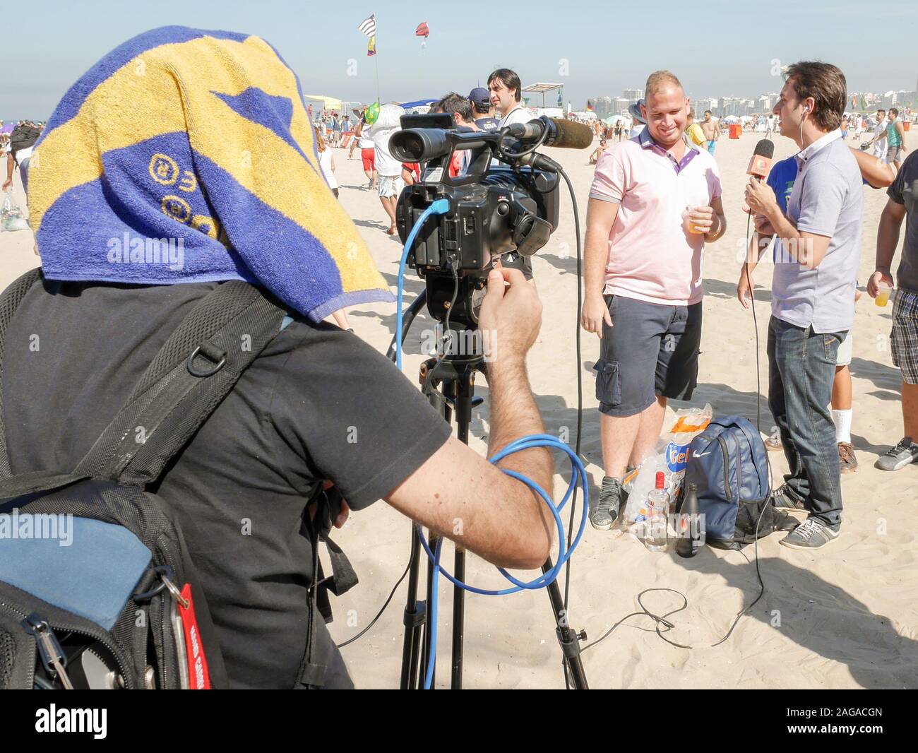 TV Interview, Rio, Brazil. A camera operator shields himself from the sun as he films a location TV interview on a Rio beach. Stock Photo