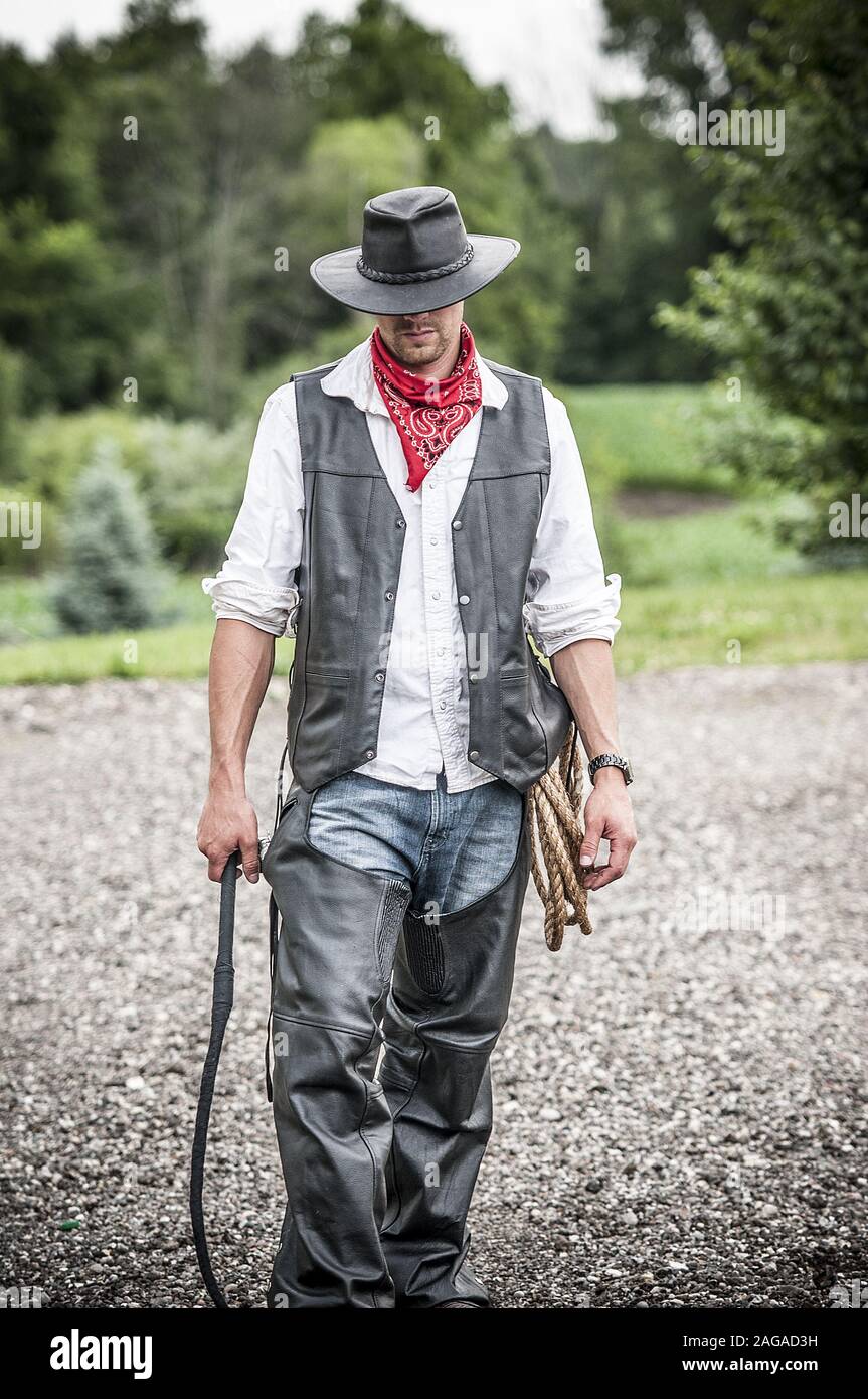 Vertical shot of a cowboy holding a whip with the rope on his side Stock Photo
