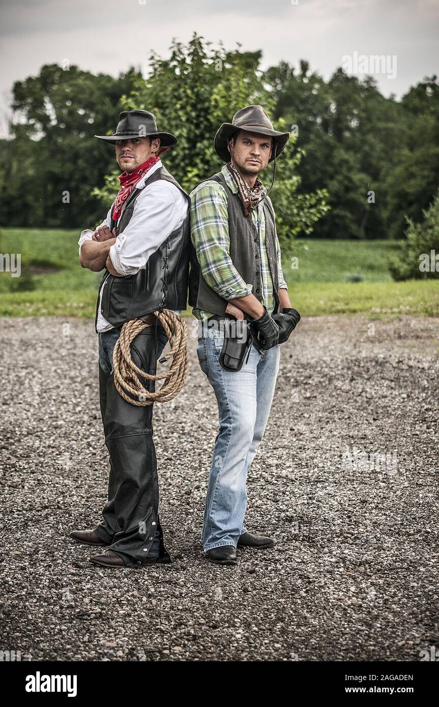 Vertical Shot Of Tow Males Wearing A Cowboy Outfit While Standing Back To Back Stock Photo Alamy