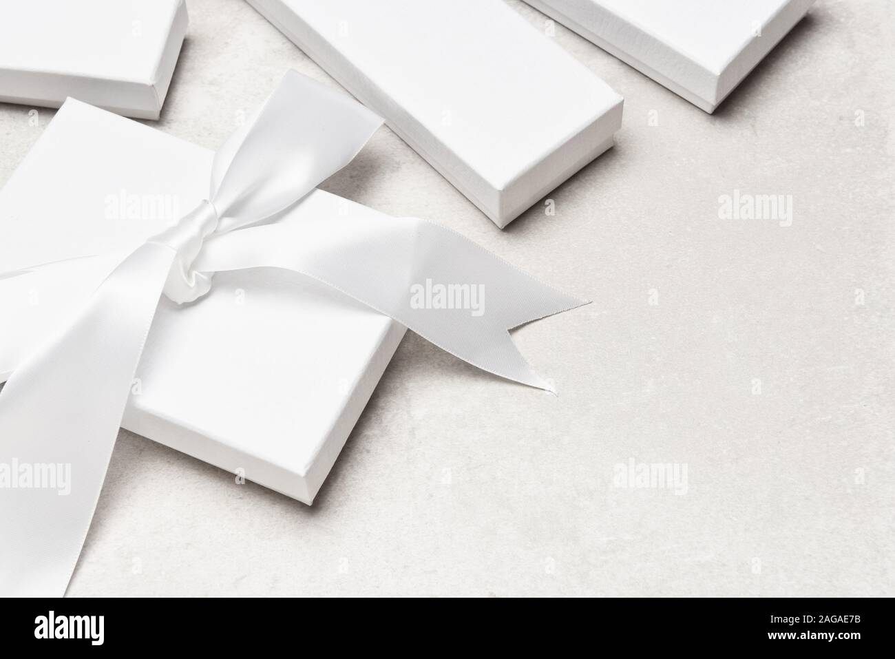 High angle shot of a group of white gift boxes on a light gray desk top. One box has a large white bow. Stock Photo