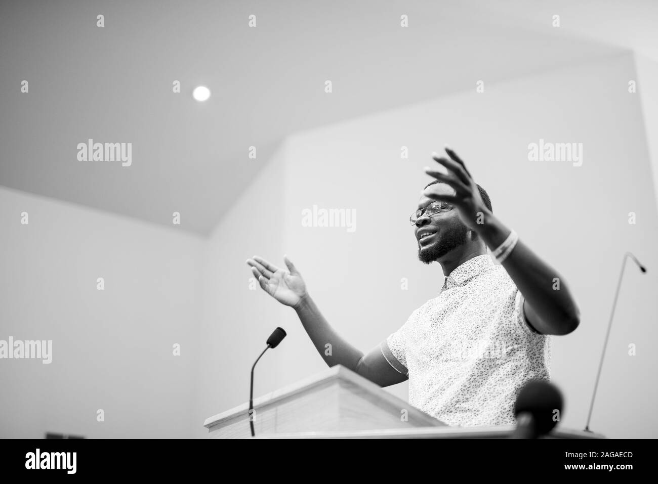 A Grayscale Shot Of A Male Taking Near A Stand With His Hands Up