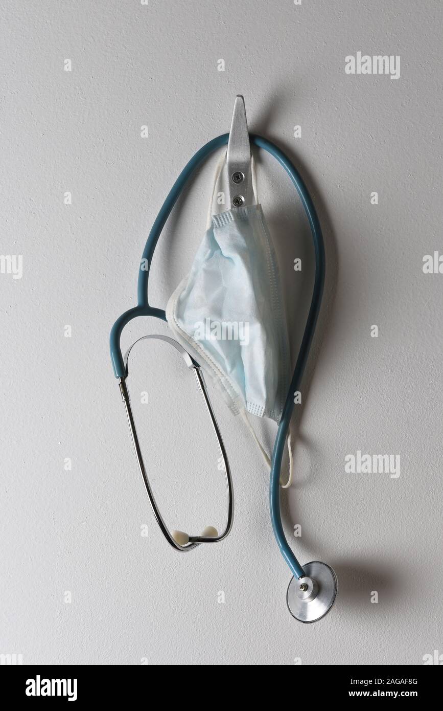 Closeup of a stethoscope and surgical mask hanging from a hook on a wall. Stock Photo
