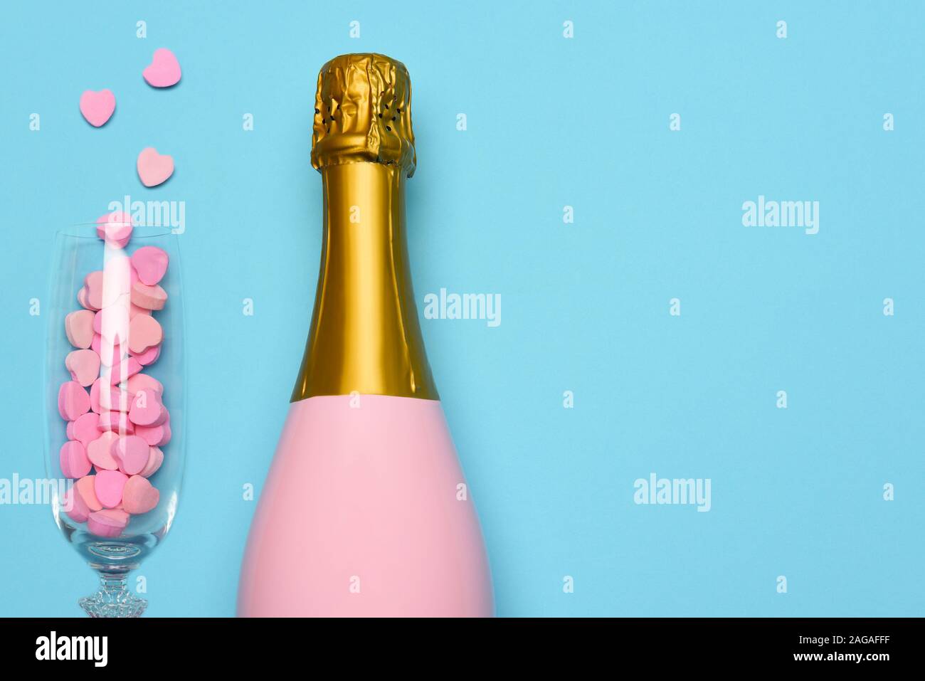 A Pink Champagne bottle and a flute with candy hearts on a blue teal background. Horizontal high angle shot with copy space. Stock Photo
