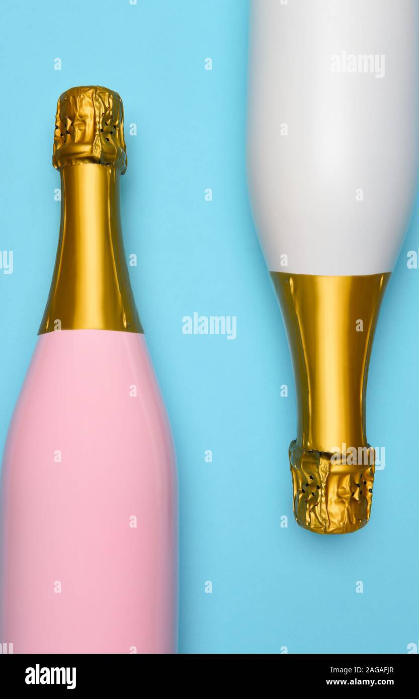 A Pink and a White Champagne bottle on a blue teal background. Vertical High angle shot. Stock Photo