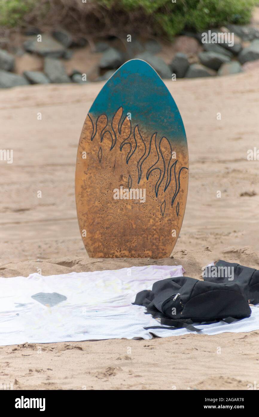 A close up view of a body, surf board in the sand next to a beach towl on a warm summers day Stock Photo