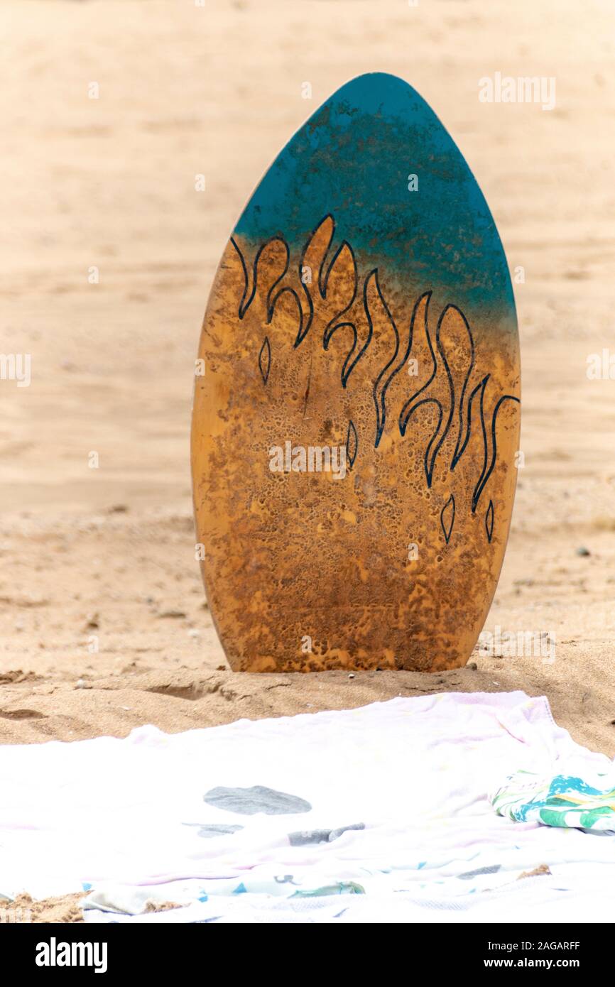 A close up view of a body, surf board in the sand next to a beach towl on a warm summers day Stock Photo