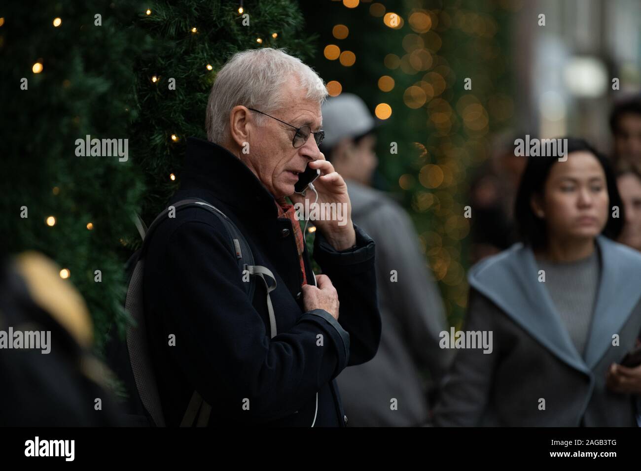 Grey haired man talking on a mobile phone, Christmas trees in the background, outside Selfridges Stock Photo