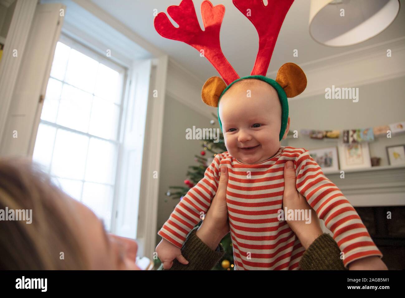 Cute baby wearing festive reindeer antlers playing with mum at christmas Stock Photo