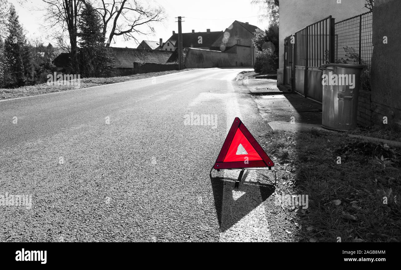 Attention! Danger on the way. Red warning triangle. Road sign on black and white village background. Caution symbol on asphalt surface. Traffic rules. Stock Photo