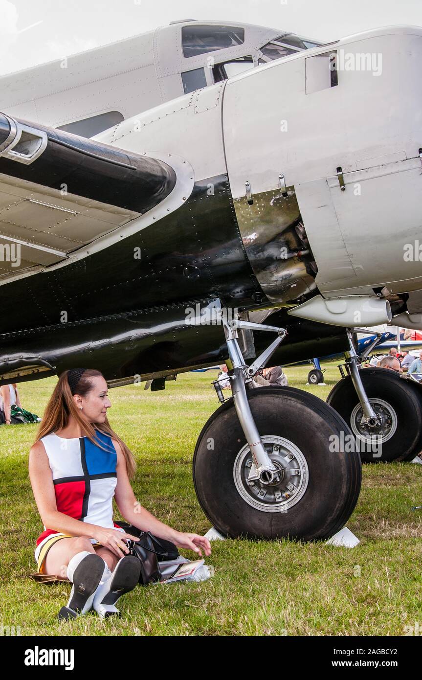 Female in period costume at the Goodwood Revival 2014. Female in period 1960s dress sitting under a vintage plane. Classic retro look. Stock Photo
