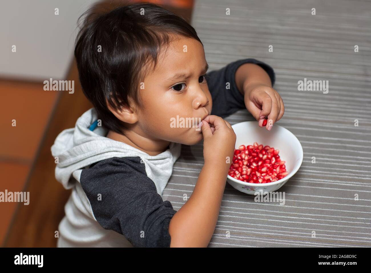 Toddler age boy tasting the sweet flavor of pomegranate seeds, self