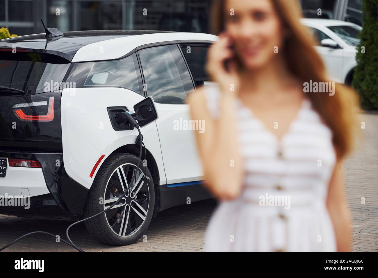Image focus technique. With phone. Woman on the electric cars charge station at daytime. Brand new vehicle Stock Photo