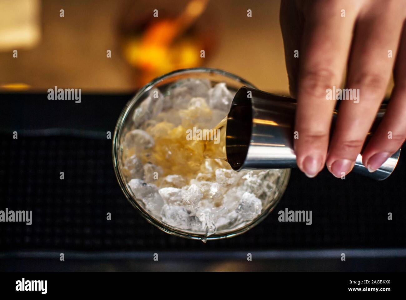 High angle closeup shot of a human hand pouring whiskey into a glass filled with ice Stock Photo