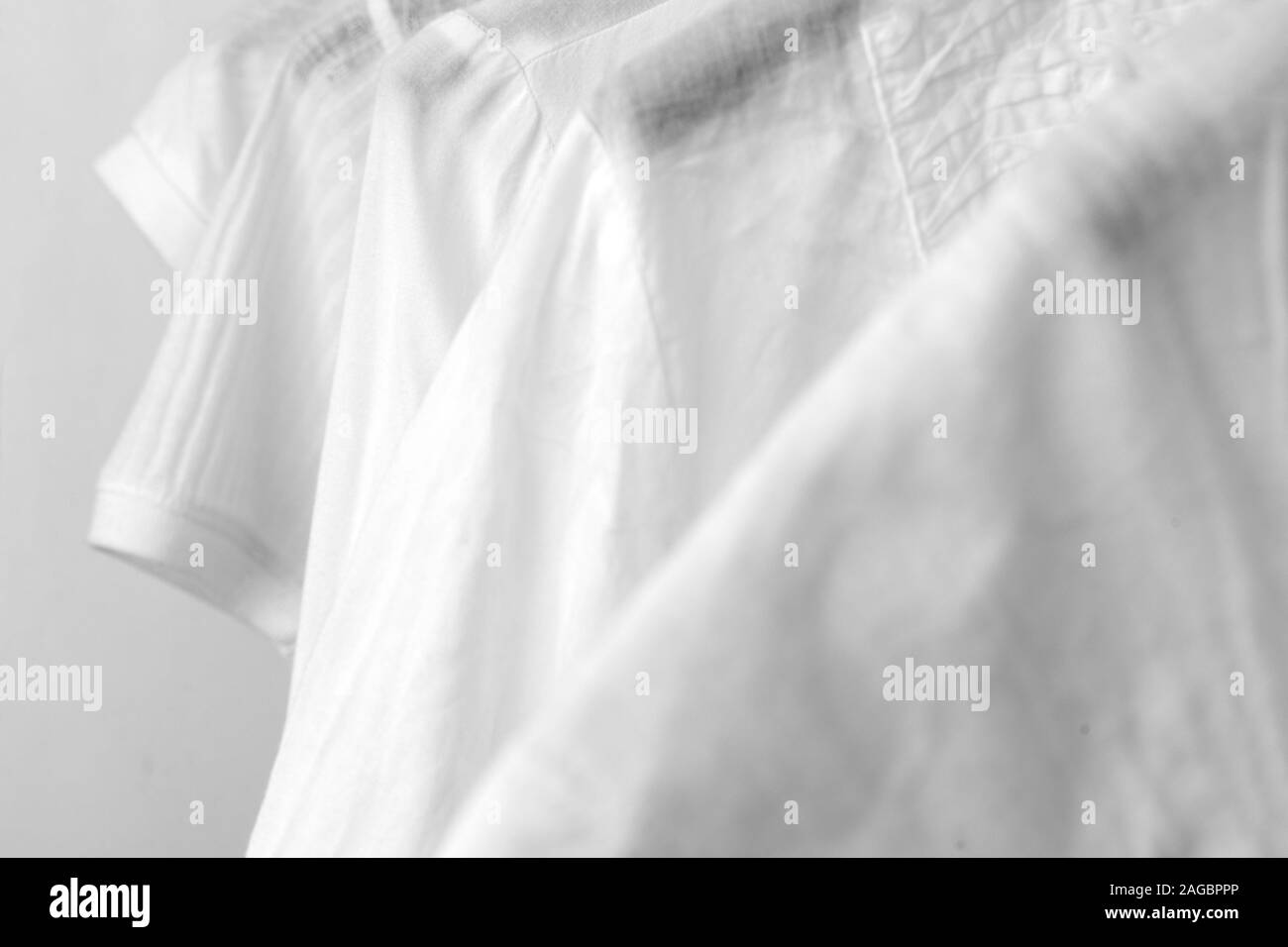 Row of white cotton clothes hang on black hangers on a rack in a shop. Woman minimalist wardrobe. Close-up. Stock Photo