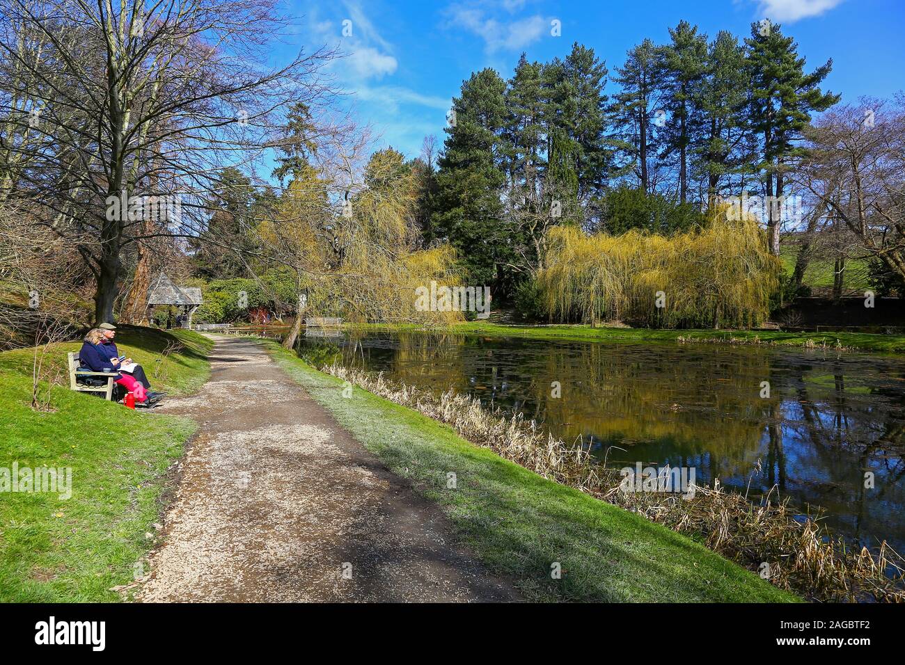 A couple sitting on a wooden bench having a picnic with the wooden Boat House in the background at Bodnant Gardens, Tal-y-Cafn, Conwy, Wales, UK Stock Photo