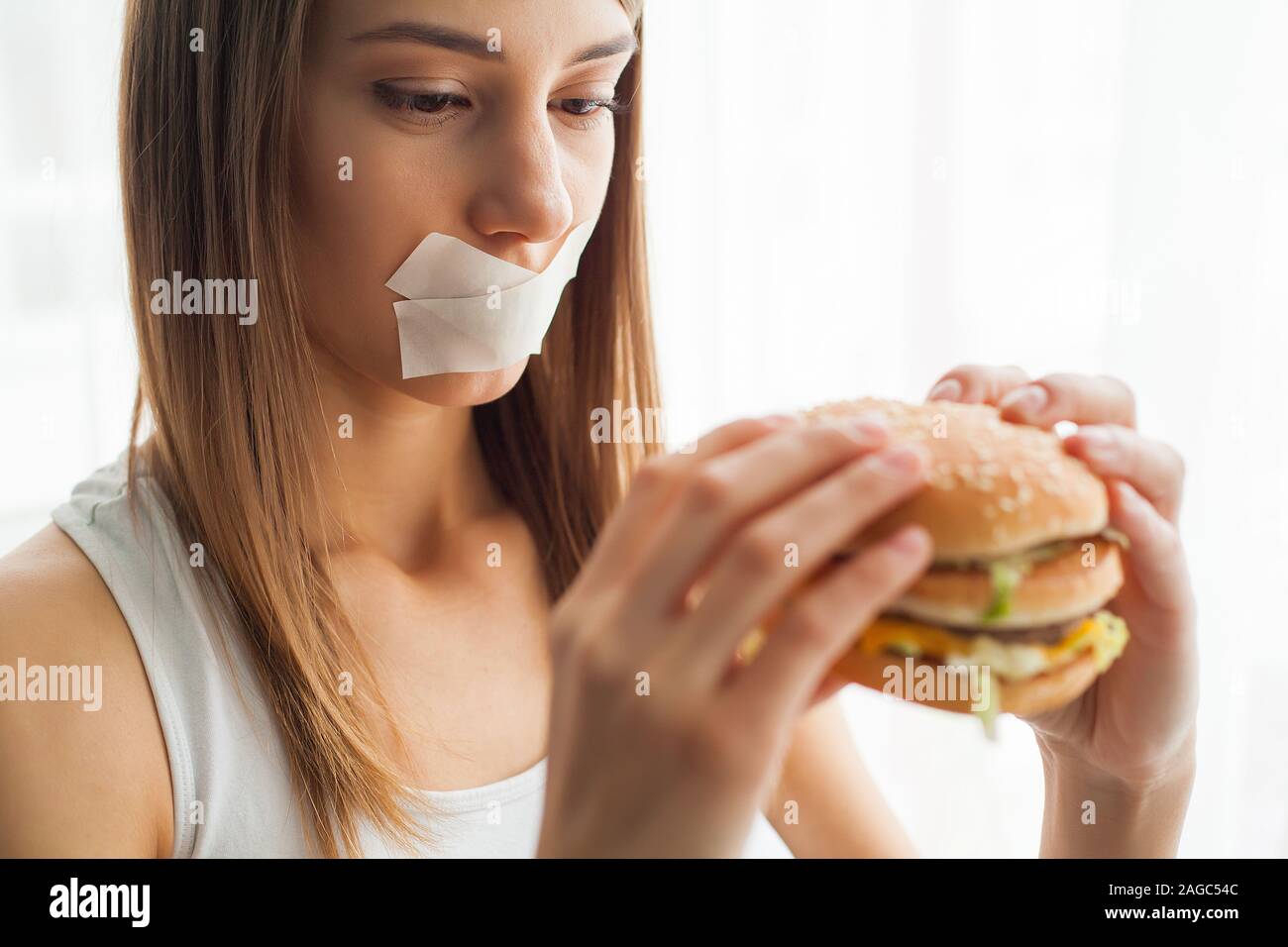 Diet. Young woman with duct tape over her mouth, preventing her to eat