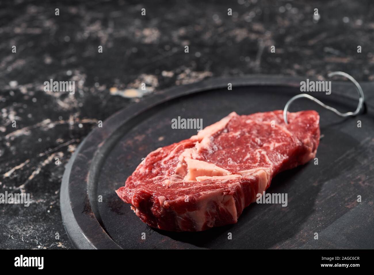 raw meat with hook on wooden plate on black marble surface Stock Photo