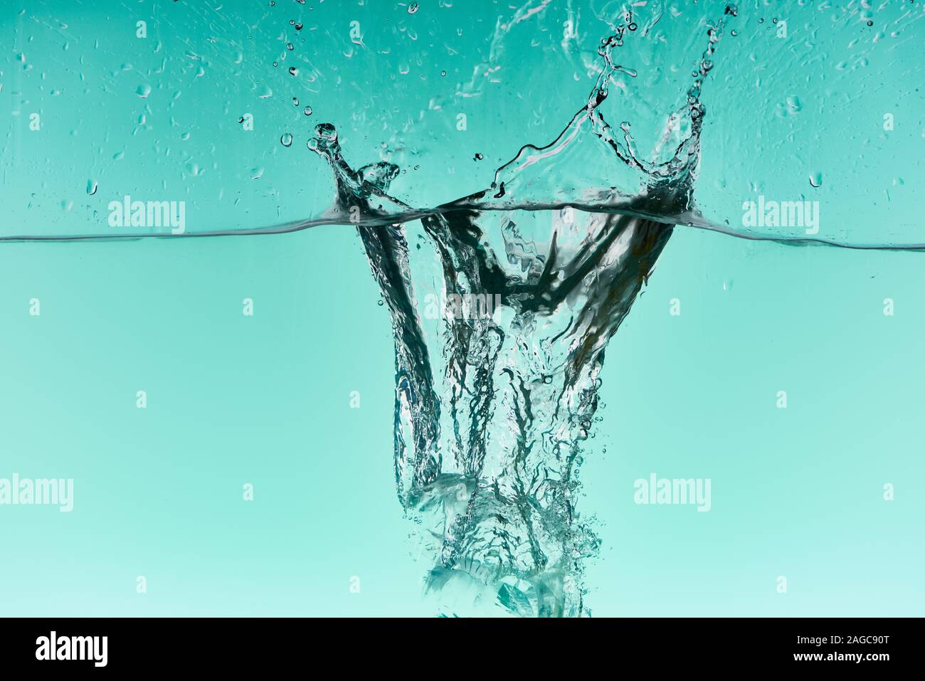 clear ice cubes falling deep in water with splash on turquoise ...